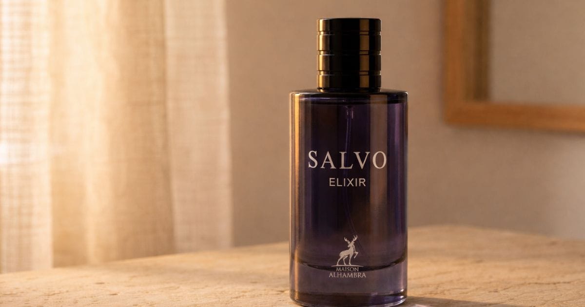 Frasco de vidro azul do perfume Salvo Elixir iluminado por luz natural suave vinda de uma janela com cortina ao fundo.